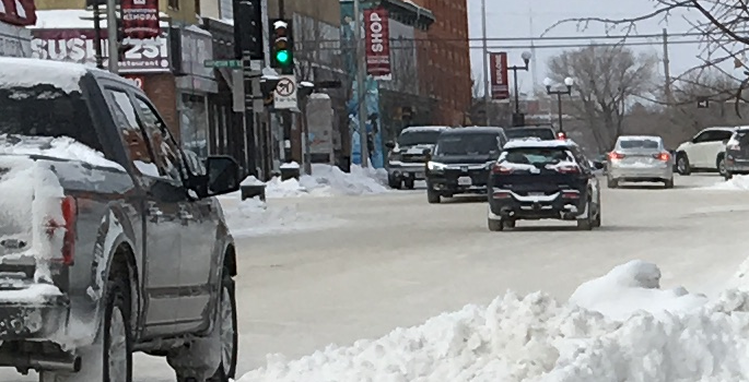 Vehicles parked along sidewalk where snow has been plowed